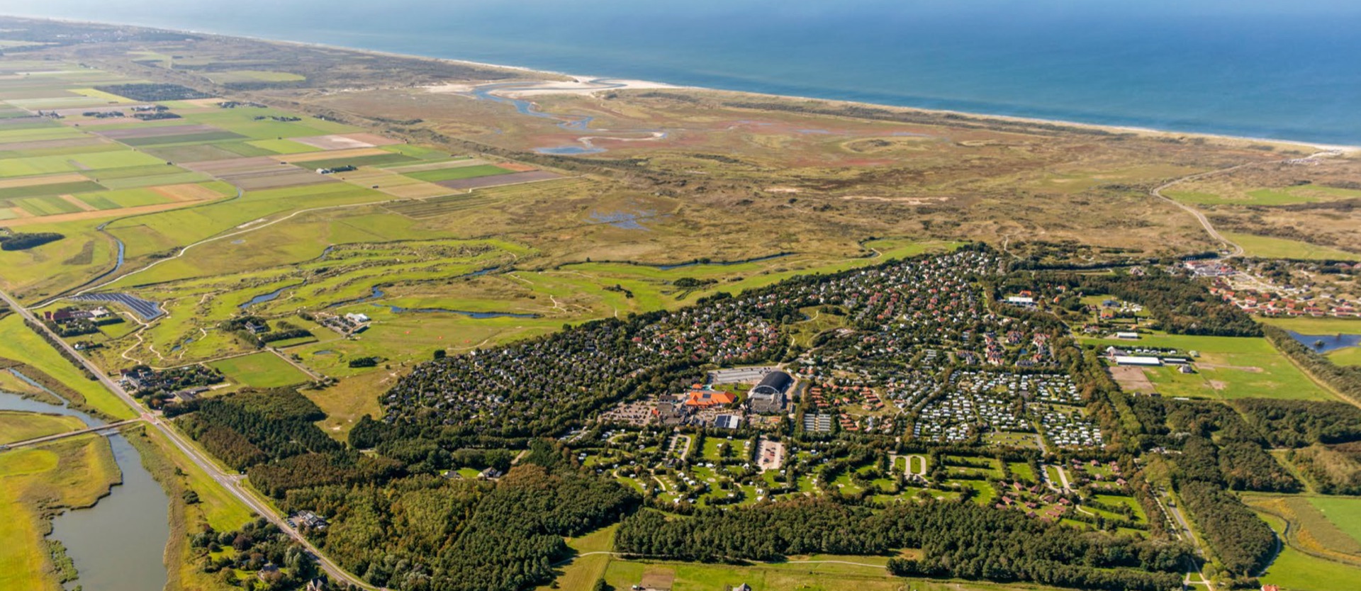 Luchtfoto van Texel: polders, duinen en een bungalowpark, met de Noordzee aan de horizon